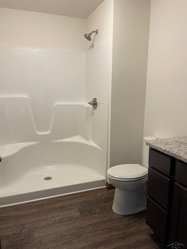 bathroom with hardwood / wood-style flooring, vanity, toilet, and a shower