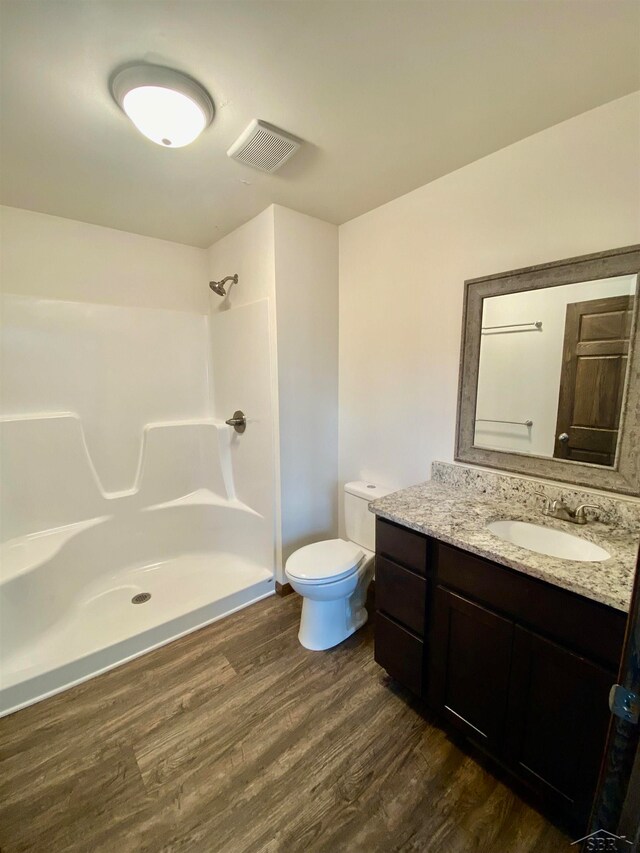 bathroom with hardwood / wood-style floors, vanity, toilet, and a shower