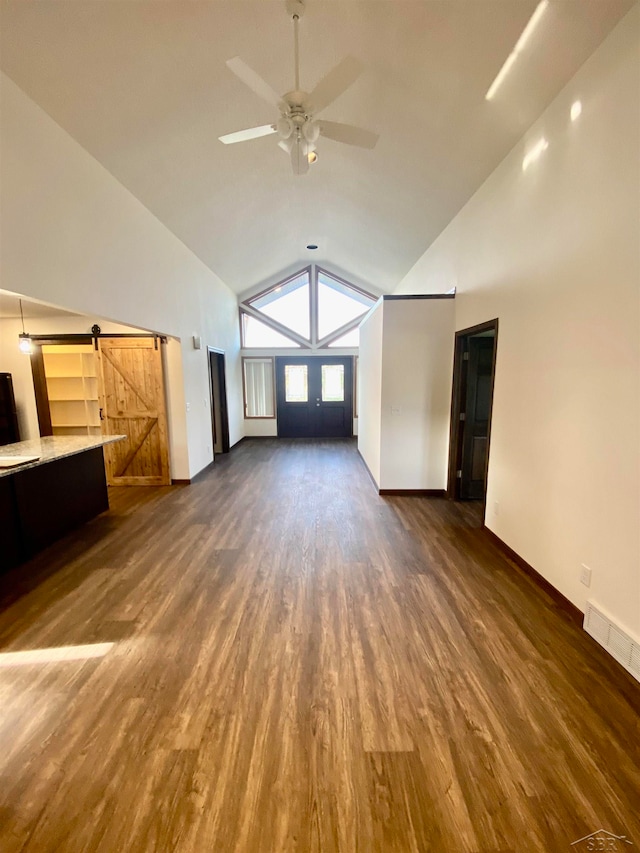 unfurnished living room featuring dark hardwood / wood-style floors, a barn door, ceiling fan, and vaulted ceiling