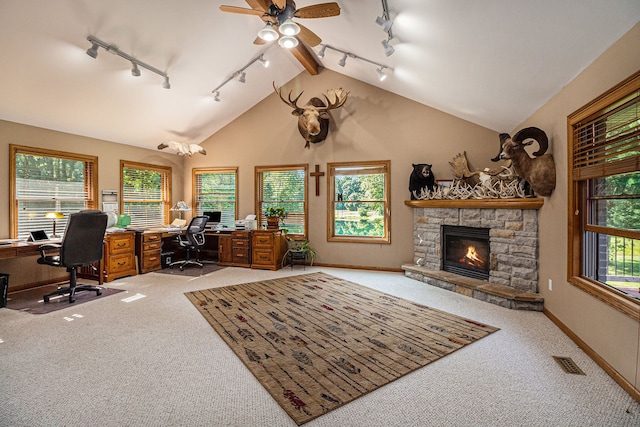 carpeted office space with a healthy amount of sunlight, a stone fireplace, lofted ceiling, and rail lighting