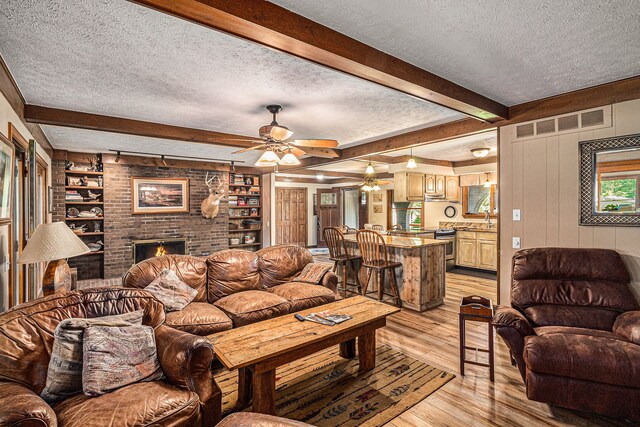 10133 W Allen Rd, Fowlerville, MI 48836 - living room featuring a textured ceiling, ceiling fan, light wood-style floors, a brick fireplace, and beam ceiling