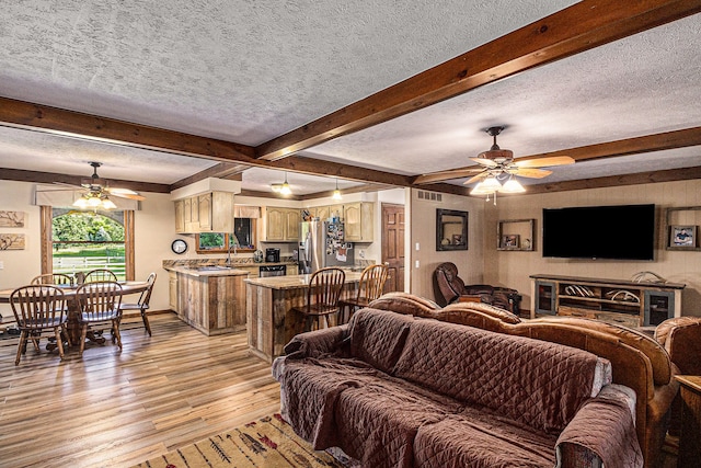 living room with beamed ceiling, a textured ceiling, light hardwood / wood-style floors, and ceiling fan