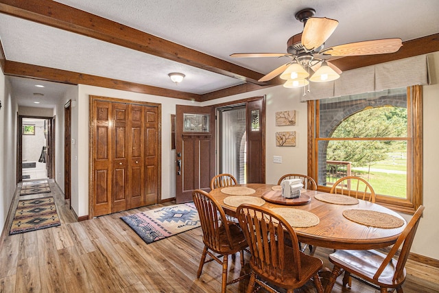 dining space with ceiling fan, beamed ceiling, a textured ceiling, and hardwood / wood-style flooring