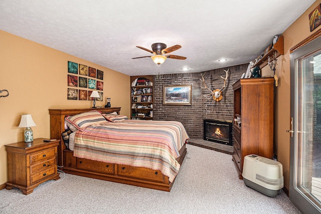 carpeted bedroom with ceiling fan, a textured ceiling, access to outside, and a brick fireplace