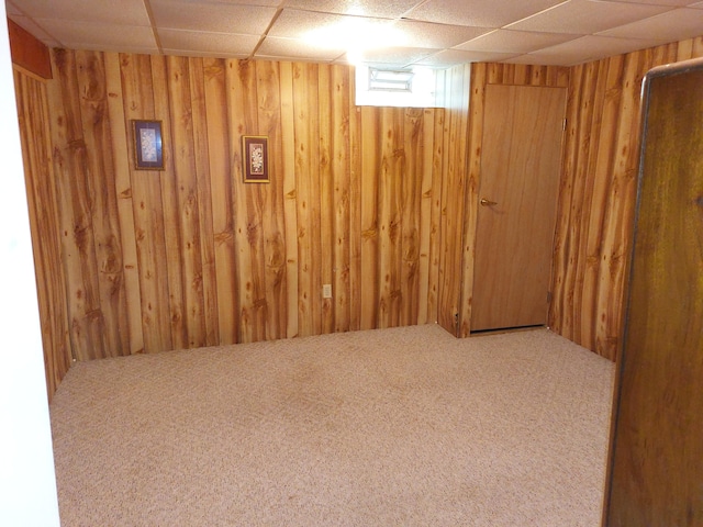 basement with a paneled ceiling, carpet floors, and wood walls