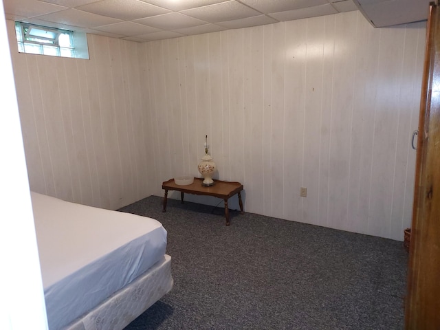 carpeted bedroom with a paneled ceiling and wood walls