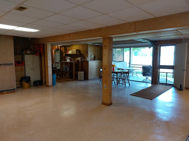 basement featuring a paneled ceiling, wood walls, and gas water heater