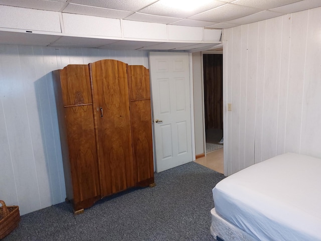 carpeted bedroom with a paneled ceiling and wood walls