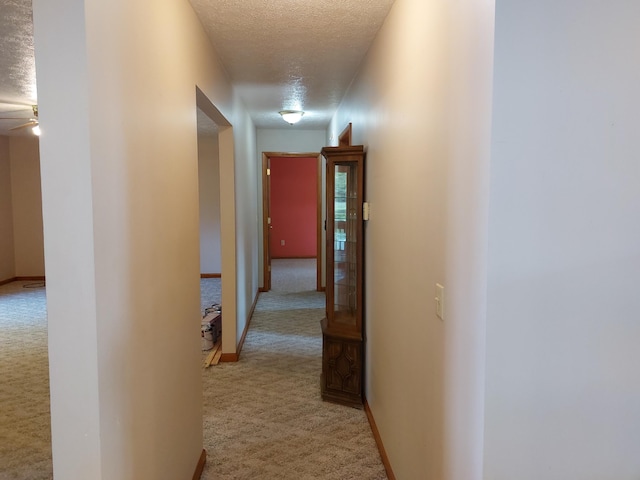 hallway with light colored carpet and a textured ceiling