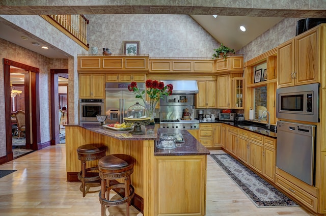 kitchen featuring light wood-type flooring, sink, built in appliances, a center island, and a breakfast bar area