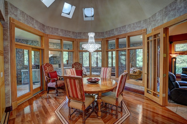 dining room featuring a notable chandelier, light hardwood / wood-style floors, high vaulted ceiling, and a skylight