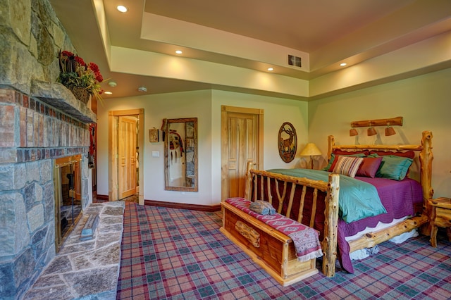 bedroom featuring carpet flooring, a tray ceiling, and a stone fireplace