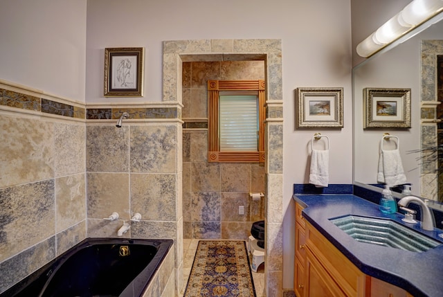 bathroom featuring tiled tub, vanity, tile walls, and toilet