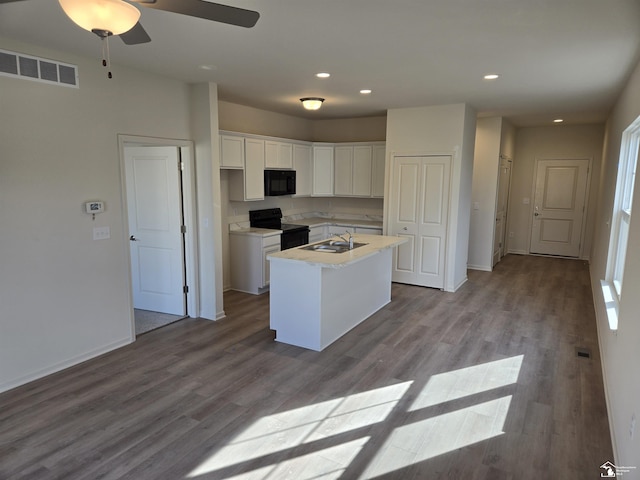 kitchen featuring light countertops, visible vents, a kitchen island with sink, white cabinets, and black appliances