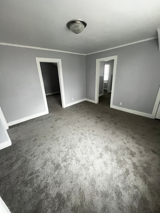 spare room with ornamental molding and dark colored carpet