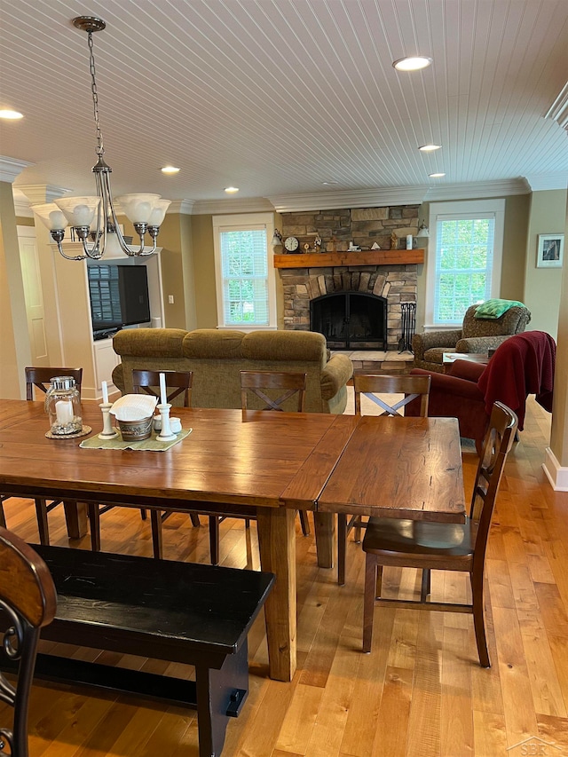 dining room featuring wooden ceiling, a stone fireplace, light hardwood / wood-style flooring, a notable chandelier, and crown molding