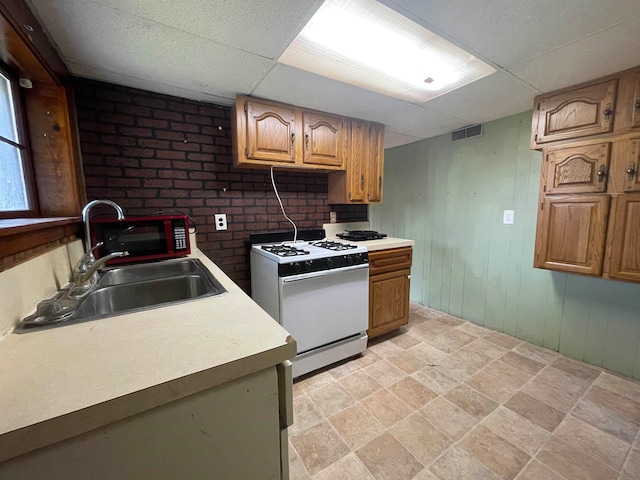 kitchen featuring white gas range, wood walls, sink, and a drop ceiling