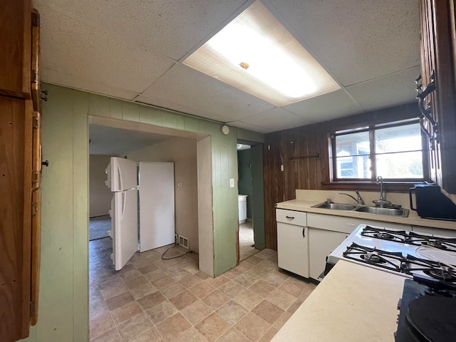 kitchen featuring a drop ceiling, white appliances, white cabinetry, and wooden walls