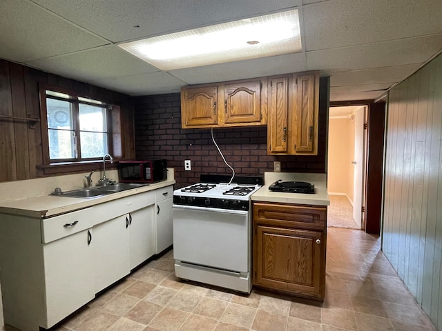 kitchen featuring white range with gas cooktop, wooden walls, sink, and a paneled ceiling