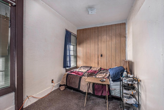 bedroom with carpet, wooden walls, and multiple windows