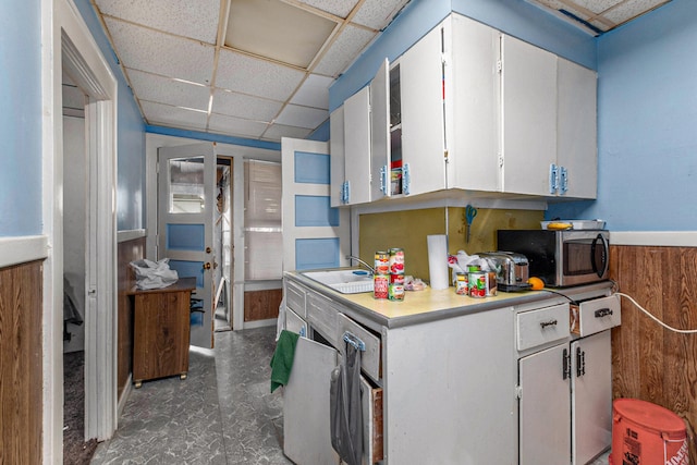 kitchen with a paneled ceiling, wood walls, white cabinetry, and sink