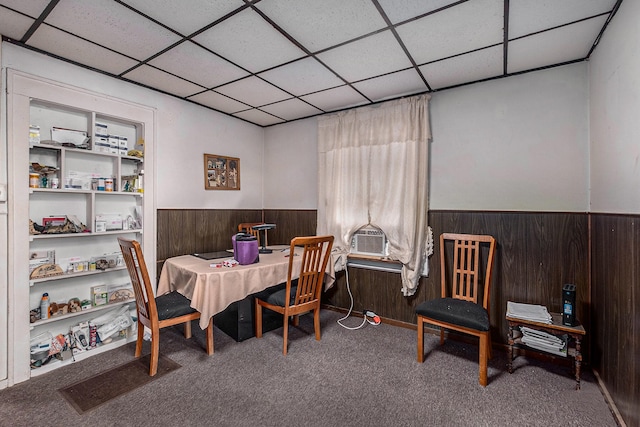 carpeted dining space featuring a drop ceiling and wood walls