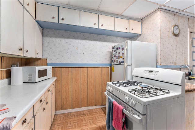 kitchen with a paneled ceiling, white appliances, and light parquet floors