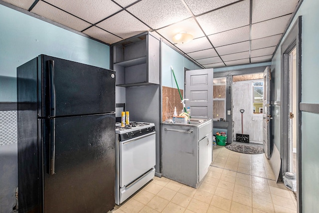 kitchen featuring a drop ceiling, black refrigerator, sink, white gas stove, and extractor fan