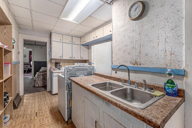 kitchen featuring a paneled ceiling, stove, light parquet floors, white cabinets, and sink