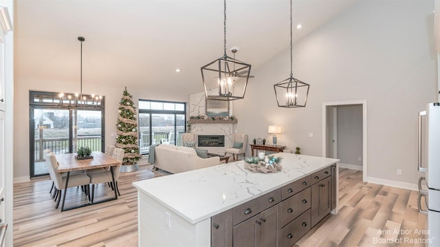 kitchen with light wood-type flooring, decorative light fixtures, high vaulted ceiling, a fireplace, and a kitchen island