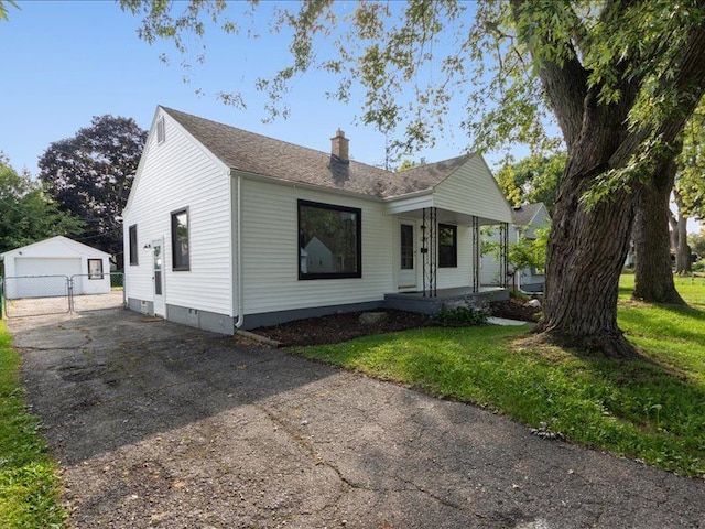 view of front of house with a garage, covered porch, an outbuilding, and a front yard