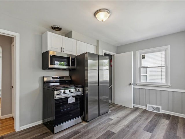 kitchen with stainless steel appliances, white cabinetry, and light hardwood / wood-style flooring