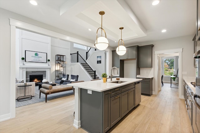 kitchen with sink, decorative light fixtures, light hardwood / wood-style flooring, dishwasher, and an island with sink