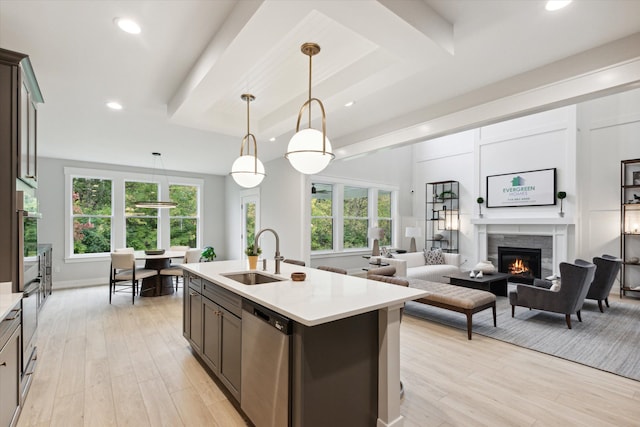 kitchen with light wood-type flooring, stainless steel dishwasher, sink, decorative light fixtures, and an island with sink