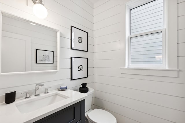 bathroom featuring wood walls, vanity, and toilet