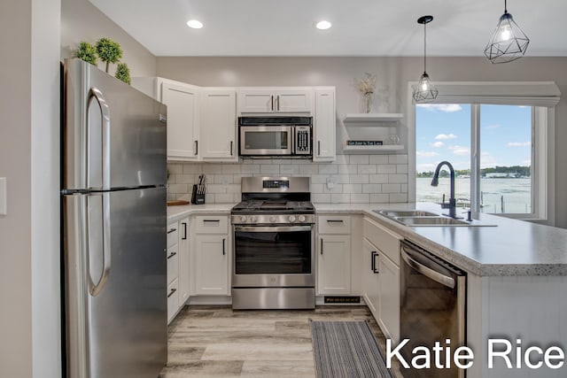 kitchen with appliances with stainless steel finishes, sink, light hardwood / wood-style floors, white cabinetry, and hanging light fixtures