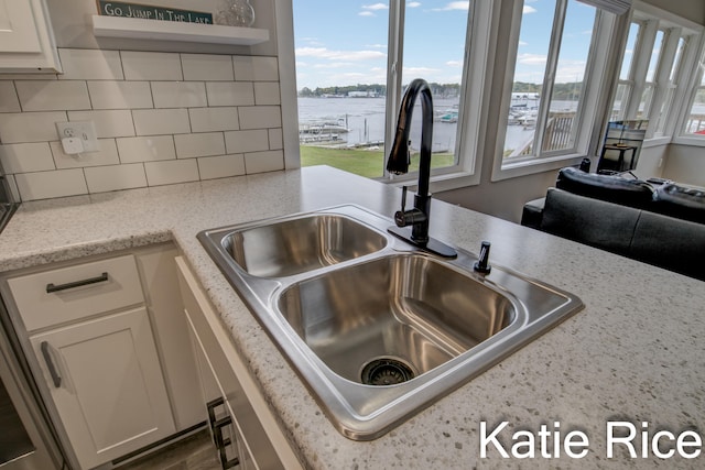 kitchen featuring sink, white cabinets, light stone counters, decorative backsplash, and a water view