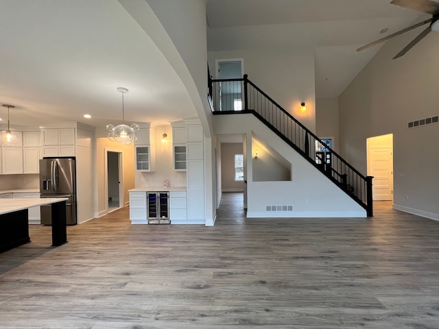 unfurnished living room with wine cooler, ceiling fan, high vaulted ceiling, and light wood-type flooring