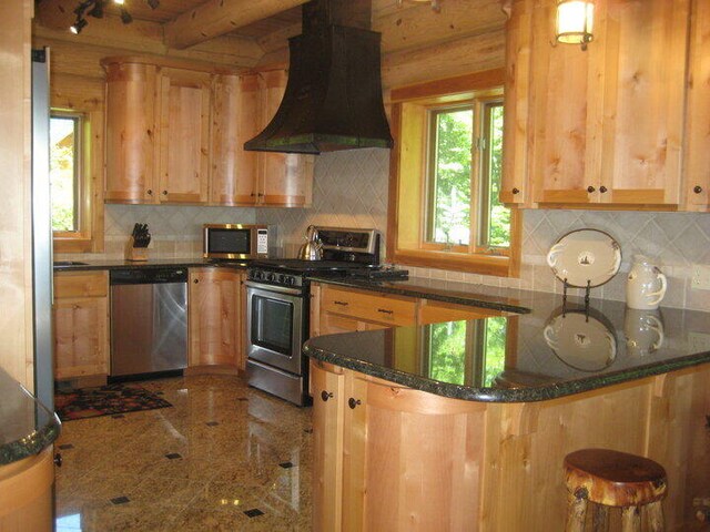 W4231 Wildwood Ln, Moran, MI 49760 - kitchen with appliances with stainless steel finishes, range hood, granite floors, a peninsula, and tasteful backsplash