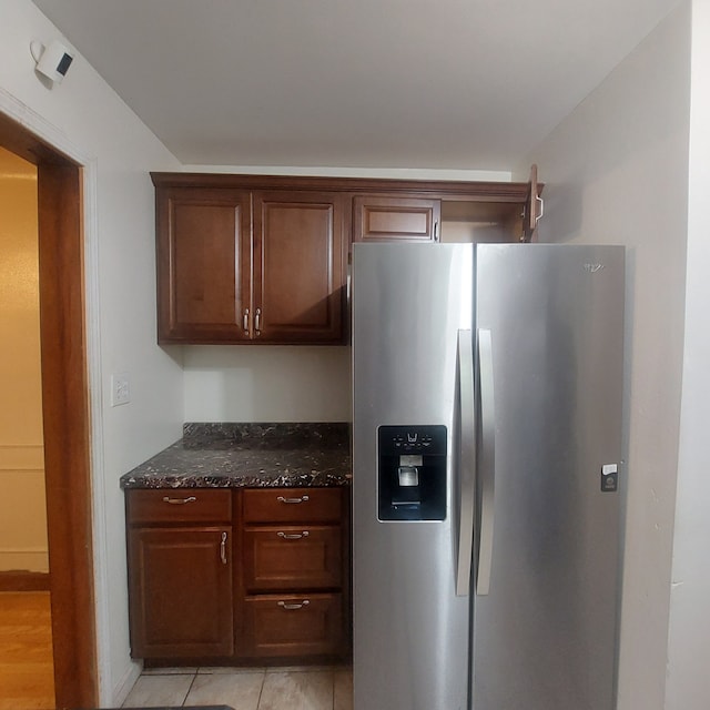 kitchen featuring stainless steel refrigerator with ice dispenser, light tile patterned floors, and dark stone countertops