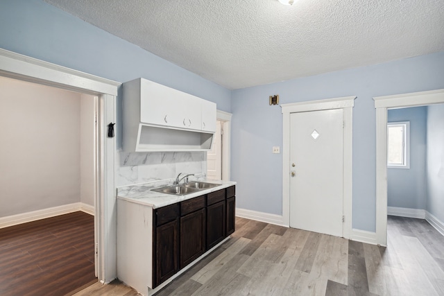 kitchen with a textured ceiling, dark brown cabinetry, light hardwood / wood-style flooring, and sink