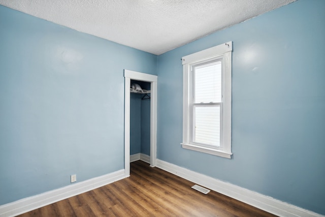 unfurnished bedroom featuring a textured ceiling, a closet, and dark hardwood / wood-style floors