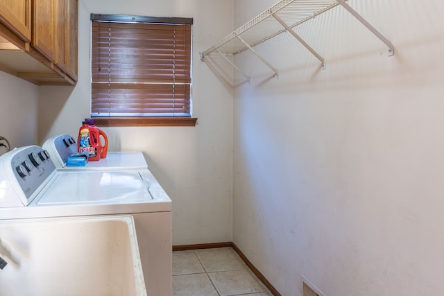 laundry room featuring washing machine and clothes dryer, light tile patterned floors, and cabinets