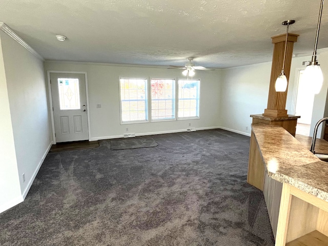 unfurnished living room with ceiling fan, sink, crown molding, a textured ceiling, and dark carpet