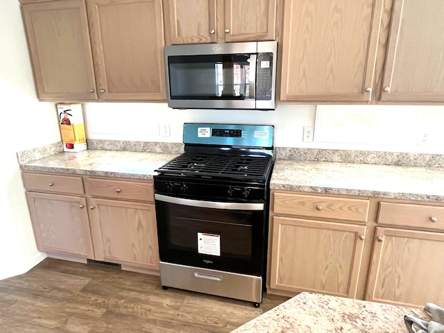 kitchen with light brown cabinetry, stainless steel appliances, and hardwood / wood-style flooring