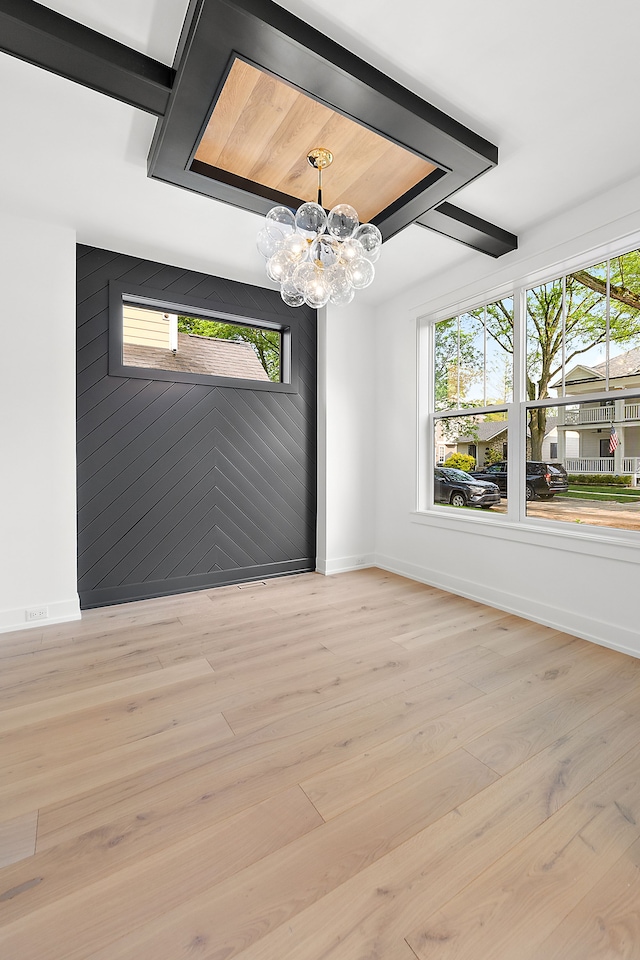 unfurnished room with light hardwood / wood-style floors, an inviting chandelier, and wooden walls