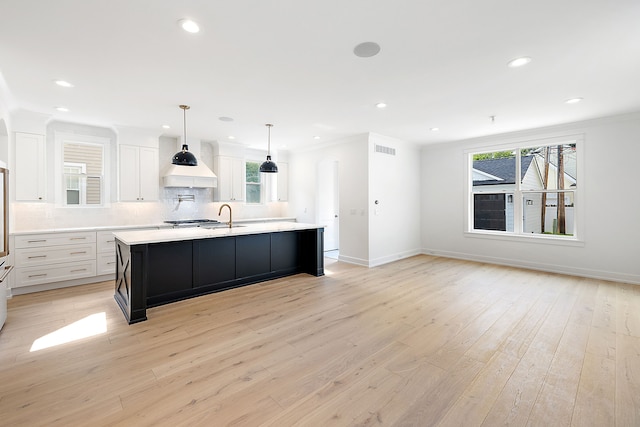 kitchen with white cabinets, a large island with sink, light hardwood / wood-style flooring, and a wealth of natural light