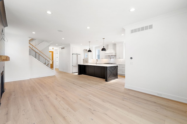 kitchen featuring pendant lighting, light hardwood / wood-style floors, high end white refrigerator, a center island with sink, and custom exhaust hood