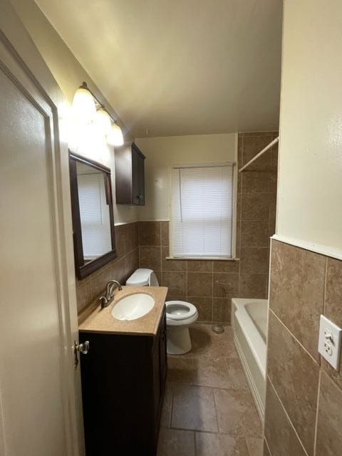 full bathroom with tiled shower / bath, vanity, toilet, and tile walls