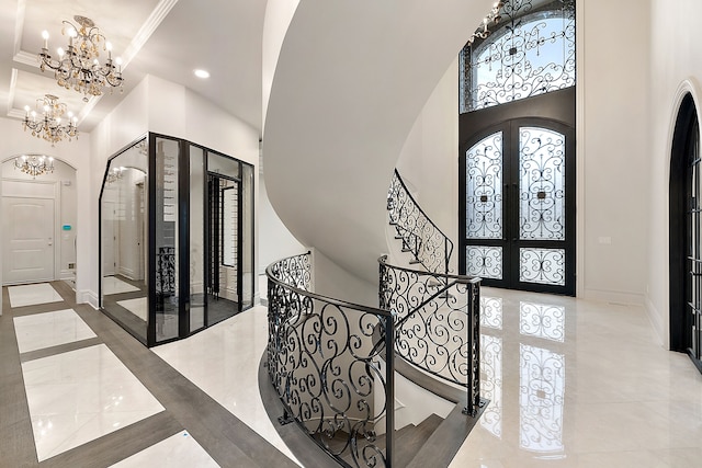 foyer featuring french doors, a towering ceiling, an inviting chandelier, and crown molding